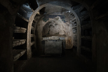 Dimly lit ancient catacomb chamber with stone shelves, altar and fresco fragments - atmospheric underground crypt in Naples, Italy