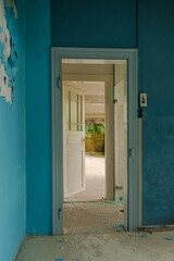 Derelict medical corridor with blue peeling paint, open vintage door and moss-covered inner room