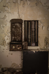 Abandoned chocolate factory time clock and numbered card rack on peeling, decayed wall