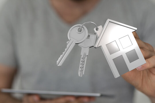 A person's hand holding a keychain with house keys and a house-shaped charm, symbolizing homeownership, real estate, and new beginnings. Perfect - Powered by Adobe