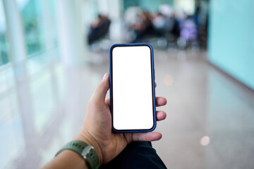 Male traveler holding a smartphone with blank screen at an airport lounge. POV closeup of hand and device clean bokeh background and reflections suggest technology, waiting and modern travel.