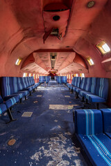 Derelict airplane cabin with blue striped seats and peeling red ceiling - abandoned aircraft interior with a long symmetrical aisle and scattered debris