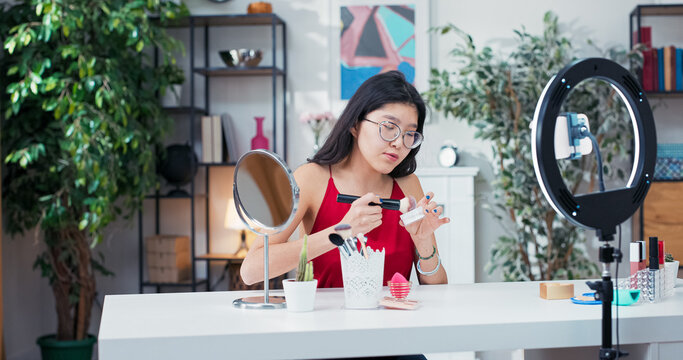 During a social media stream, the beauty blogger reviews a cosmetic product, applying rice powder to her skin with a soft brush while discussing its benefits. - Powered by Adobe