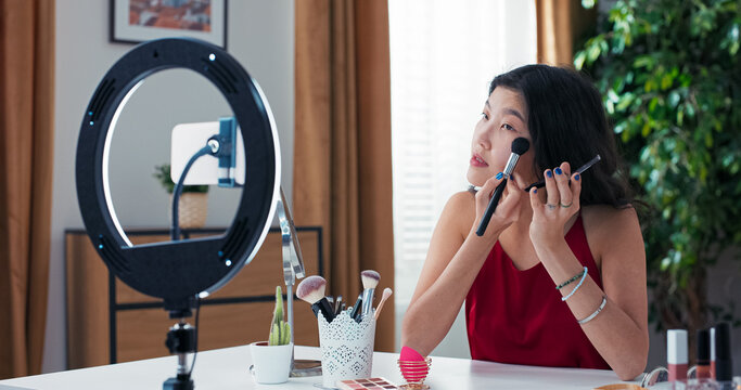 A talented woman with a gentle appearance streams live on social media. She applies bronzer and shares contouring tips with her followers.