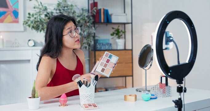 A makeup content creator demonstrates her daily eye look, filming a cosmetics review with a phone and ring light, talking to viewers on live stream.