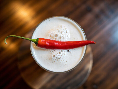 Craft cocktail with vibrant red chili pepper garnish, a spicy twist on classic mixology, perfect for culinary blogs and restaurant menus, top view!