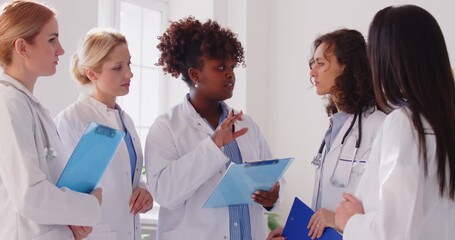 Happy positive african american chief female doctor explaining, talking to diverse medical team, professional colleagues standing together in clinic, team discussing patient diagnosis, mentoring - Powered by Adobe