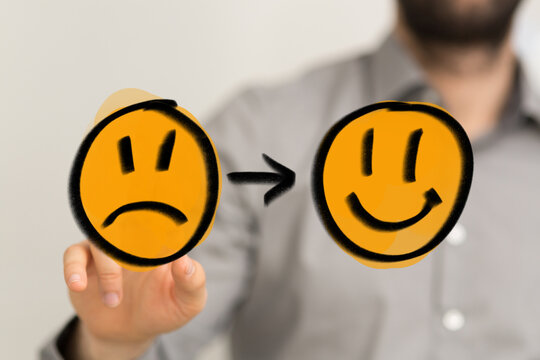 Conceptual image showing a hand changing a sad emoji to a happy one, symbolizing positive emotional transformation, personal growth, and overcom