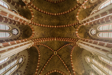 Symmetrical vaulted ceiling of a historic monastic church with red-brick ribbed vaults and stained glass windows