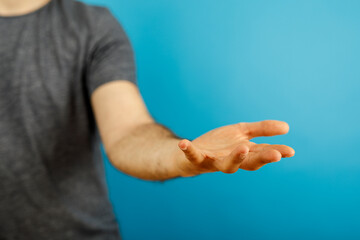 Fototapeta premium Close-up of a person's hand extended forward, palm open. Against a vibrant blue backdrop, the image suggests giving, receiving, or an offer of