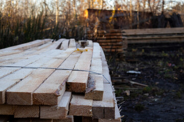 Planks of wood are stacked in a lumber yard, illuminated by the soft morning light as the day begins, ready for construction projects