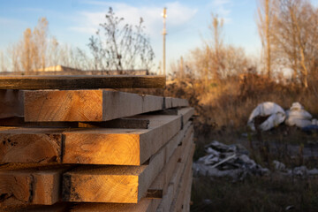 Wooden planks are stacked neatly in an industrial area, surrounded by autumn foliage and debris in...