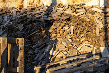 Stacked wooden planks and pallets create a large pile in a yard, illuminated by the warm light of...