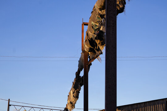 A long, rusted pipeline extends upward from a metal support, set against a clear blue sky in the afternoon light of early autumn