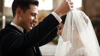 Smiling groom gently lifts the veil of his bride during their wedding ceremony.