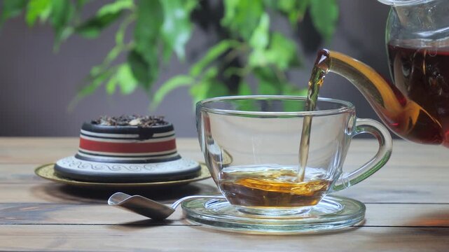 Black tea is poured into a light-colored cup from a teapot.