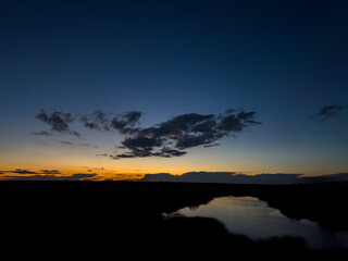 Fototapeta premium Golden sunset horizon with dark clouds and a reflective river creating a tranquil and atmospheric evening landscape.