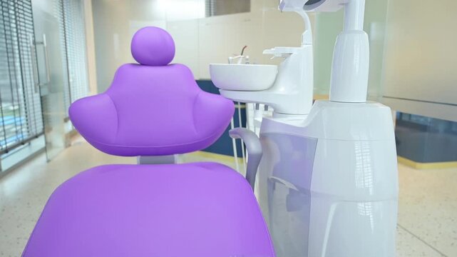 he dentist places the tweezers on the purple dental treatment chair, which is part of the clinic&rsquo;s fully equipped dental unit with vertical shot