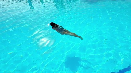 Tranquil swimming scene, Gentle diver gliding peacefully along water, Serene aquatic performer moving smoothly through sunlight, Calm swimmer gracefully glides across bright sunlit water surface
