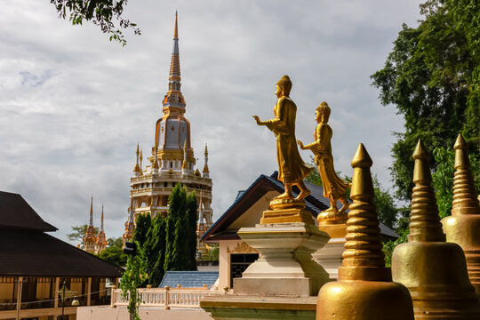 A pair of elegant golden Buddha statues stand beside small stupas, with the grand, ornate pagoda of the famous Wat Tham Suea (Tiger Cave Temple) rising beautifully in background in Krabi, Thailand.
