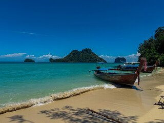 Obraz premium Traditional wooden long-tail boats are moored on golden sand of Poda Island, as gentle turquoise waves wash ashore under clear blue sky. A classic travel and transportation scene from Krabi, Thailand.
