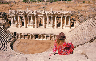 A tourist in a beautiful red dress at the historical monument of the theater of the ancient city of Hierapolis