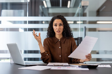 Businesswoman feeling stressed and overwhelmed, sitting at her office desk with laptop and documents, experiencing confusion and frustration with a complex work challenge