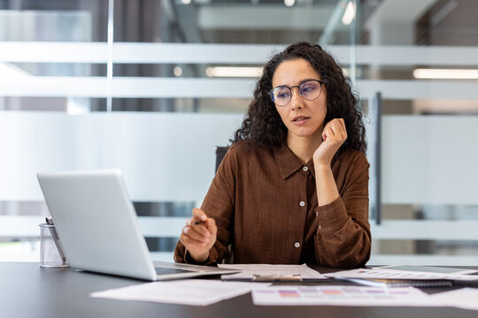 Businesswoman intently focusing on her laptop screen and documents, analyzing data and developing new strategies while working at a modern office desk