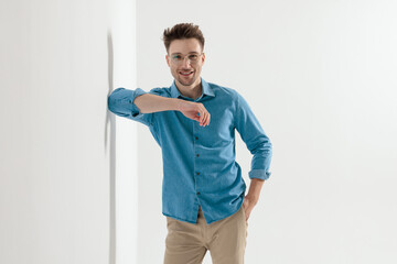 Happy young casual man smiling and leaning elbow on wall