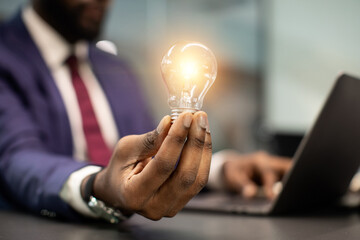 Unrecognizable african american businessman with illuminated light bulb, working on laptop at...