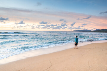 Naklejka premium Tourist walking alone on sandy beach at sunset, enjoying beautiful ocean view in kauai, hawaii