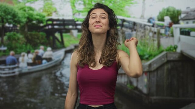 Woman smiles and points finger at canal and tour boat beside lush plants in street scene; invitation excitement.