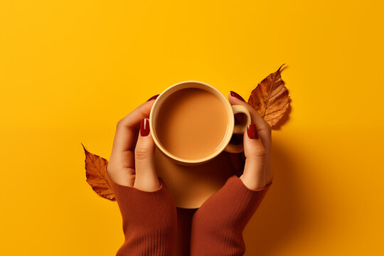 Mains tenant une tasse de boisson chaude sur fond jaune uni avec feuilles d&rsquo;automne s&egrave;ches, ambiance chaleureuse et espace n&eacute;gatif copyspace, visuel saisonnier pour campagne culinaire ou marketing