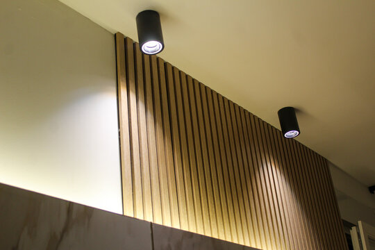 Two ceiling spotlights illuminating a wooden slat wall, creating a stylish and cozy atmosphere in a modern interior space.