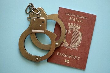 Malta passport with police handcuffs on table close up. Criminal level and arrests in Europe concept