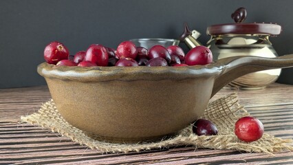 Brown bowl with red cranberries on burlap, teapot and cup in the background. 