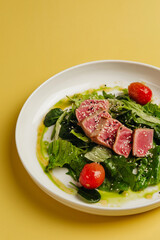 Fresh salad with tuna fillet and green leaves on a yellow background is very cheerful