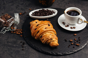 A large airy croissant with chocolate on a dark background tempts coffee