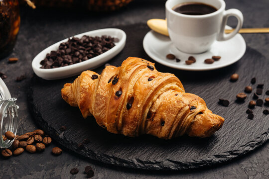 A large airy croissant with chocolate on a dark background tempts coffee