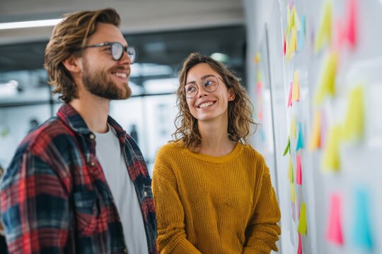 Young business professionals brainstorming ideas on a whiteboard covered in sticky notes in a modern office, collaborating on a new strategy together and smiling.