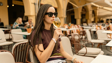 Beautiful woman enjoying a glass of wine seated in a very pleasant outdoor setting. Relaxing atmosphere, sunny day, and leisure lifestyle moment.