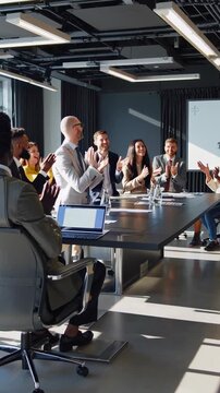 executives applauding in modern boardroom, CEO smiling while team stands around long table with laptops and swivel chairs, sunlit windows, glass walls, focused professionals in suits, collaborative