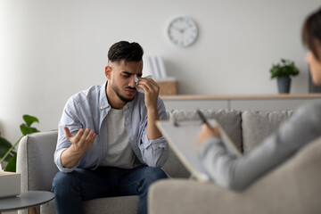 A middle eastern man is sitting on a couch in a therapist's office, visibly upset and crying. He is sharing his feelings and struggles during a counseling session with a professional psychologist.