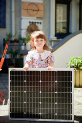 Cute girl holding portable solar panel and smiling. Green lifestyle from the youngest. Concept of green energy generation.