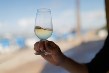 Hand holding glass of manzanilla sherry enjoying beach view