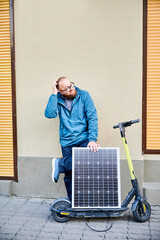 Male person holds photovoltaic solar panel, for charging electric scooter in urban settings. Integration of solar power as sustainable energy source, promoting eco-friendly urban transportation.