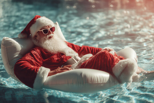 Santa Claus takes a relaxing break from his holiday duties lounging on an inflatable in a swimming pool wearing sunglasses