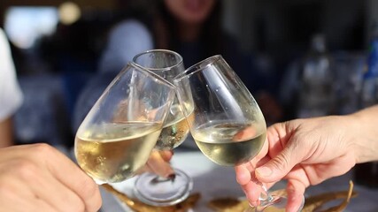 Group of people celebrating and toasting with white wine glasses during a meal at a restaurant - Powered by Adobe