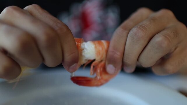 Male hands carefully peeling the shell off a cooked sanlucar prawn over a white plate