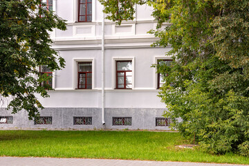 The elegant facade of a two-story historic building with white stone walls and a stone sidewalk. It's a warm autumn day.